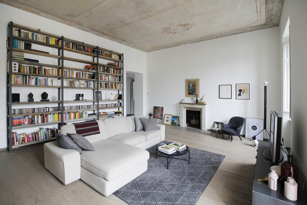 This is an example of an expansive industrial enclosed living room in Turin with a library, white walls, a standard fireplace, a stone fireplace surround, a freestanding tv, light hardwood floors and beige floor.