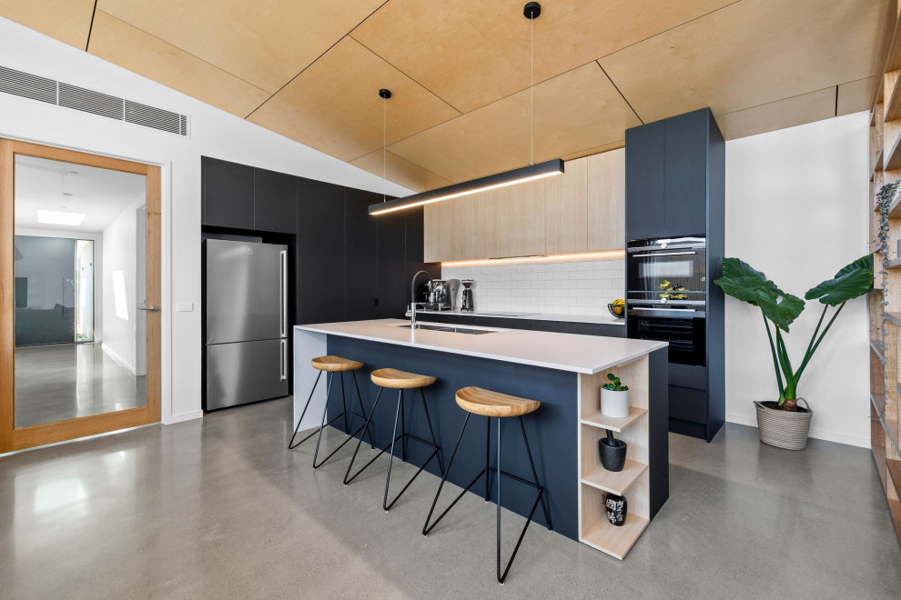 Example of a mid-sized trendy l-shaped concrete floor, wood ceiling and gray floor open concept kitchen design in Geelong with an undermount sink, flat-panel cabinets, black cabinets, quartz countertops, white backsplash, subway tile backsplash, black appliances, an island and white countertops