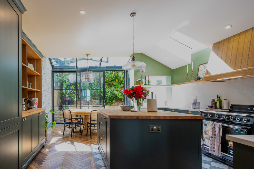 Inspiration for a classic u-shaped kitchen/diner in London with green cabinets, white splashback, stone slab splashback, black appliances, medium hardwood flooring, an island, brown floors, white worktops, a vaulted ceiling and shaker cabinets.