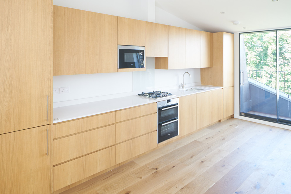 Mid-sized modern single-wall kitchen in London with an integrated sink, flat-panel cabinets, light wood cabinets, solid surface benchtops, light hardwood floors and no island.