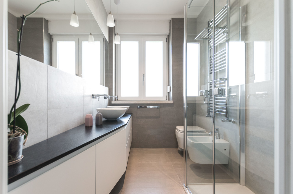 Mid-sized contemporary bathroom in Cagliari with grey walls, porcelain floors, flat-panel cabinets, white cabinets, a bidet, a vessel sink, a hinged shower door, black benchtops, beige tile, gray tile and beige floor.