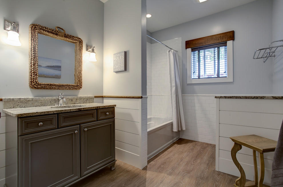 Country master bathroom in Grand Rapids with medium wood cabinets, a drop-in tub, a shower/bathtub combo, a one-piece toilet, grey walls, medium hardwood floors and a drop-in sink.