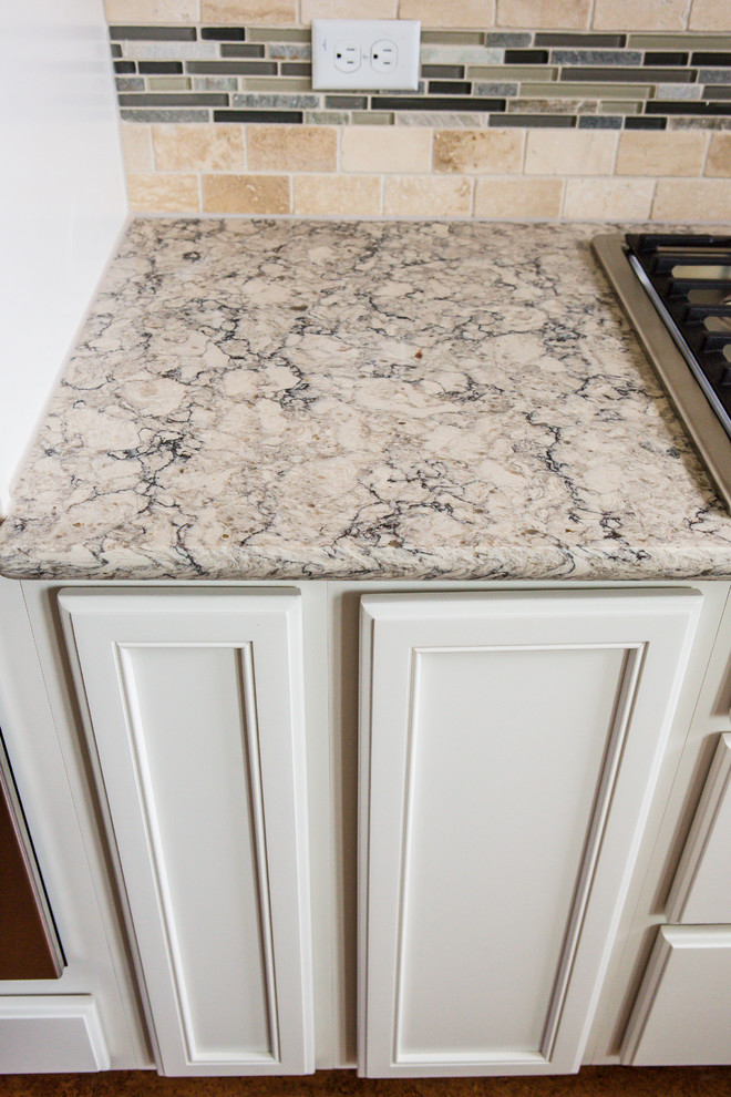 Example of a mid-sized transitional l-shaped medium tone wood floor eat-in kitchen design in Austin with an undermount sink, recessed-panel cabinets, white cabinets, granite countertops, beige backsplash, stone tile backsplash, stainless steel appliances and an island