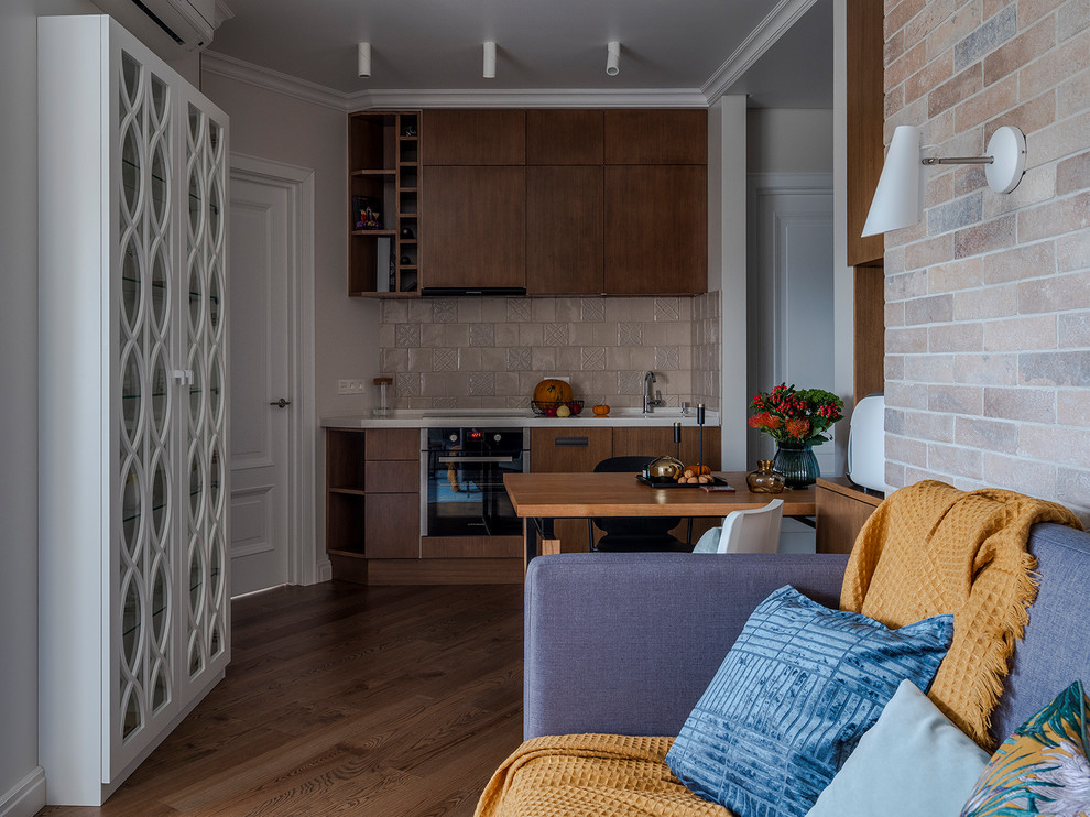 Mid-sized contemporary single-wall open plan kitchen in Moscow with flat-panel cabinets, medium wood cabinets, solid surface benchtops, beige splashback, ceramic splashback, black appliances, medium hardwood floors, no island, brown floor and white benchtop.