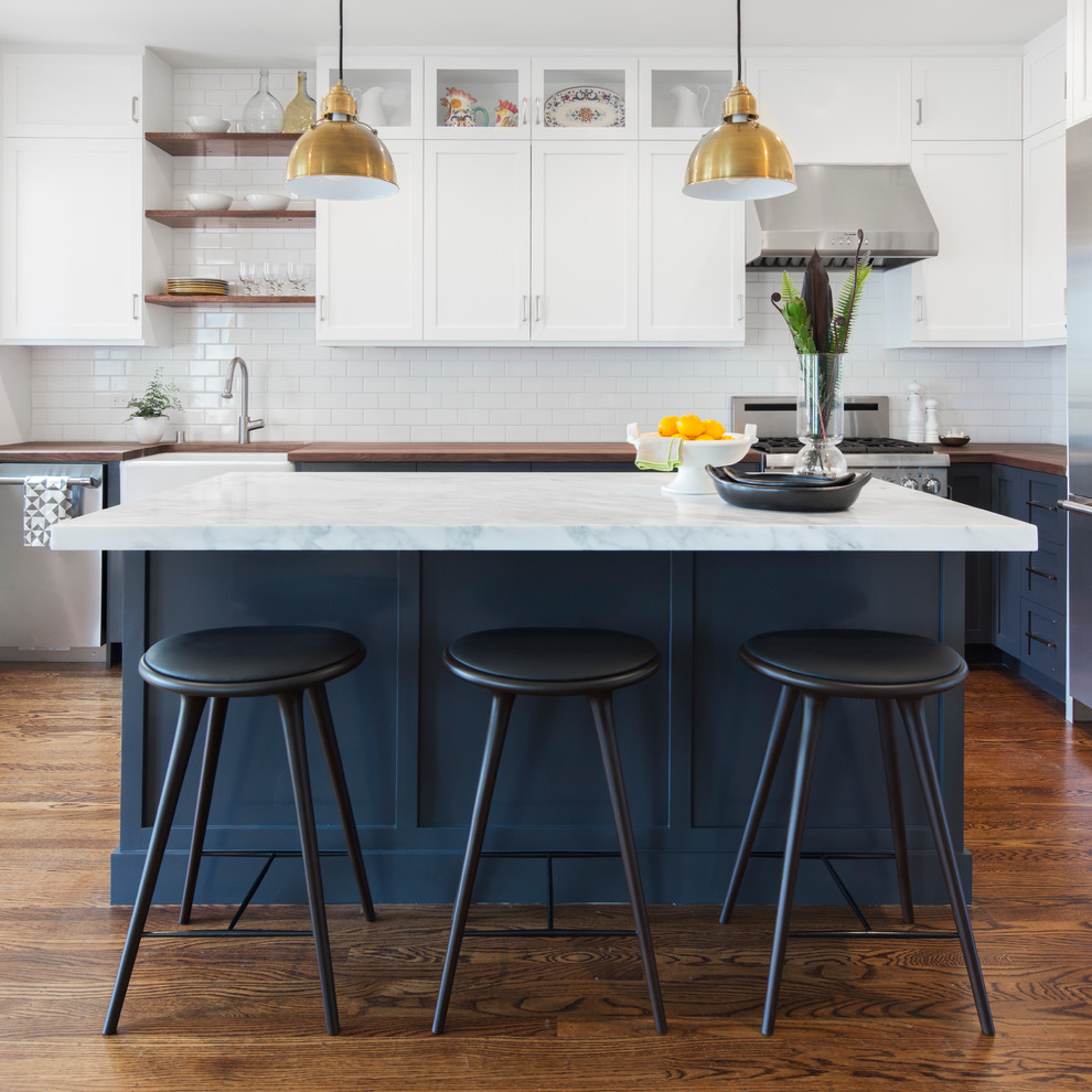 Inspiration for a transitional l-shaped kitchen in San Francisco with a farmhouse sink, shaker cabinets, white cabinets, wood benchtops, white splashback, subway tile splashback, stainless steel appliances, dark hardwood floors and with island.
