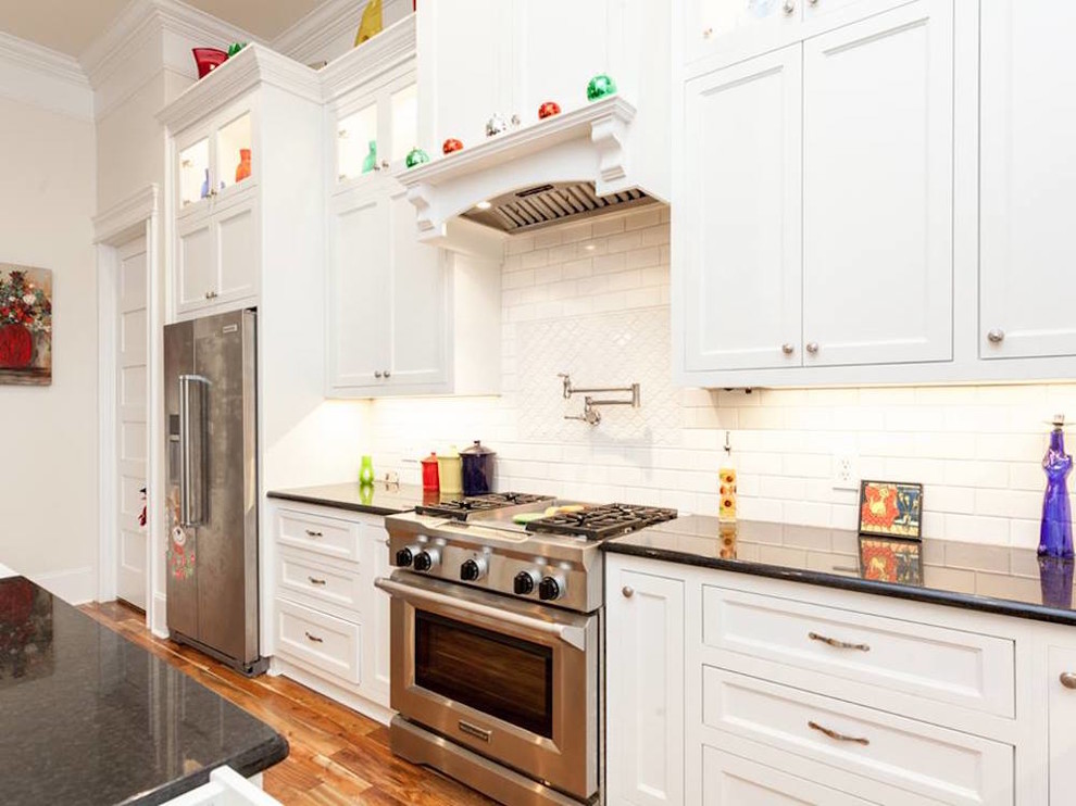 Example of a large transitional u-shaped medium tone wood floor and multicolored floor open concept kitchen design with a farmhouse sink, recessed-panel cabinets, white cabinets, quartz countertops, white backsplash, subway tile backsplash, stainless steel appliances, an island and black countertops