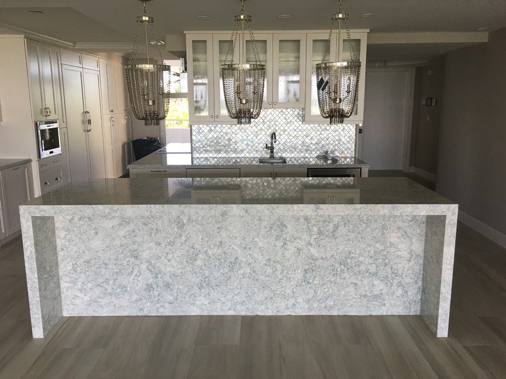 Inspiration for a large transitional l-shaped light wood floor and beige floor kitchen remodel in Miami with an undermount sink, shaker cabinets, white cabinets, quartzite countertops, gray backsplash, glass tile backsplash, stainless steel appliances and an island