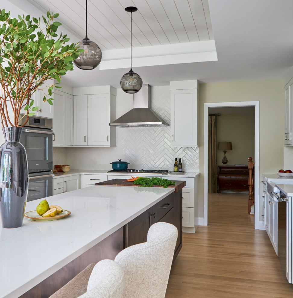 Eat-in kitchen - large transitional u-shaped light wood floor, brown floor and coffered ceiling eat-in kitchen idea in Chicago with a farmhouse sink, shaker cabinets, white cabinets, quartz countertops, white backsplash, subway tile backsplash, stainless steel appliances, an island and multicolored countertops