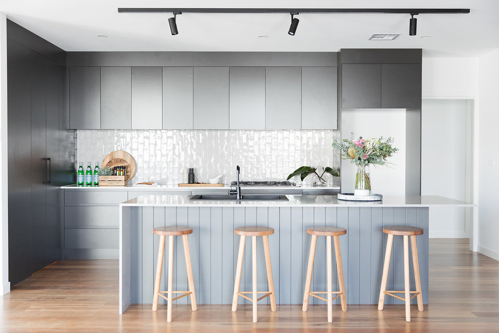 Inspiration for a mid-sized modern galley open plan kitchen in Canberra - Queanbeyan with a double-bowl sink, black cabinets, quartz benchtops, grey splashback, subway tile splashback, black appliances, medium hardwood floors, with island and brown floor.