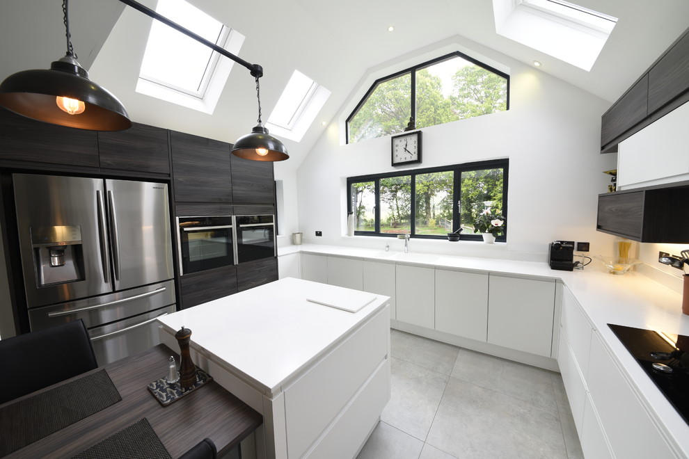 Photo of a large modern u-shaped eat-in kitchen in Kent with a drop-in sink, flat-panel cabinets, white cabinets, solid surface benchtops, white splashback, panelled appliances, porcelain floors, with island and grey floor.