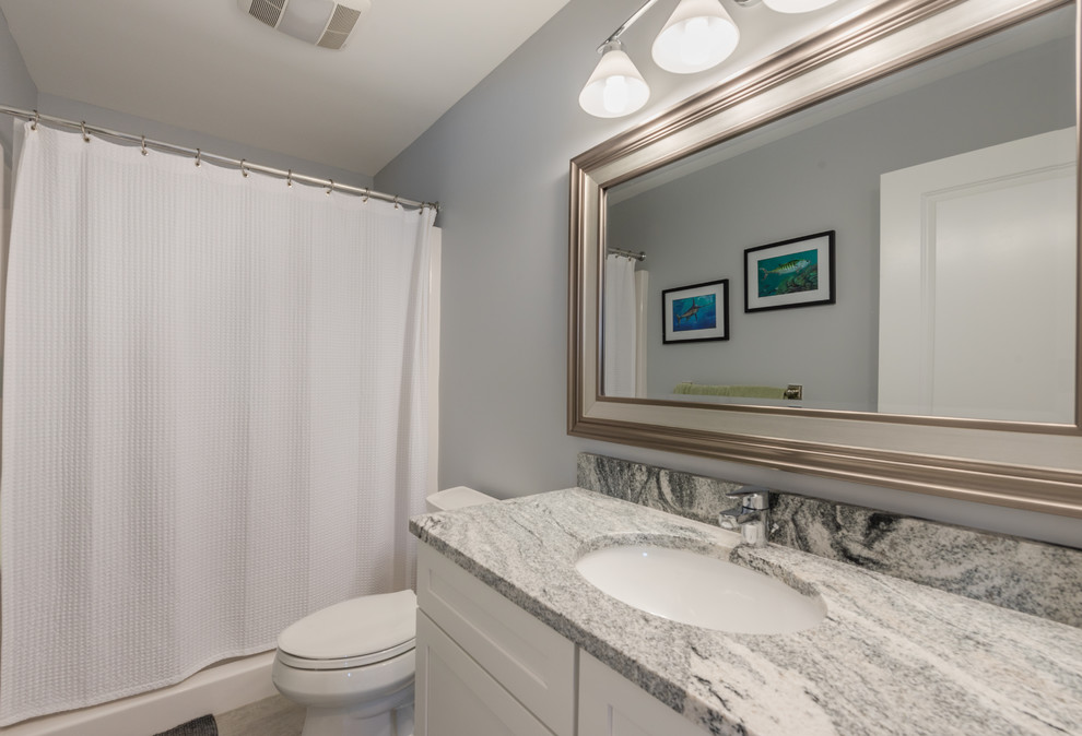 This is an example of a mid-sized transitional 3/4 bathroom in New York with shaker cabinets, white cabinets, an alcove tub, a shower/bathtub combo, a two-piece toilet, grey walls, limestone floors, an undermount sink, quartzite benchtops, beige floor and a shower curtain.