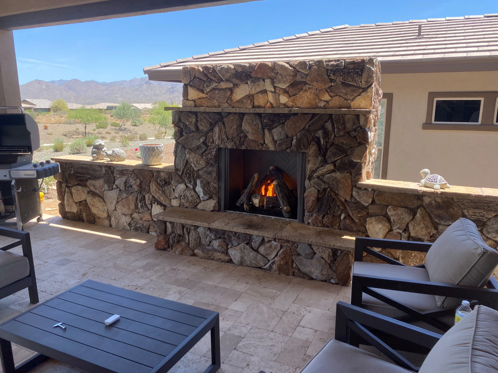 Example of a large mountain style backyard stone patio design in Phoenix with a fireplace and a roof extension