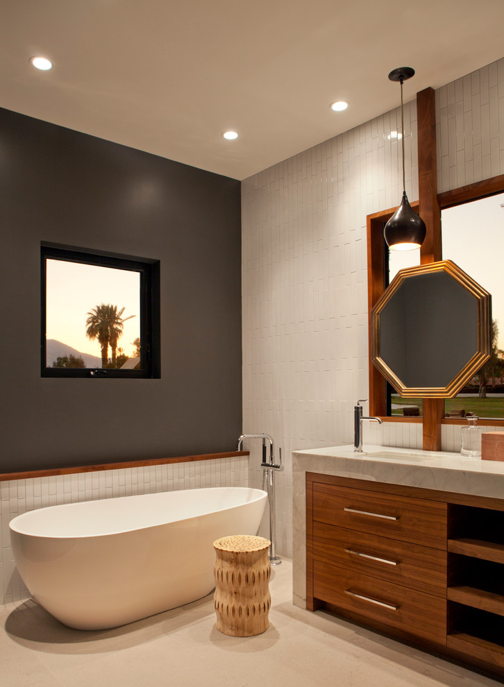 This is an example of a mid-sized midcentury master bathroom in Los Angeles with flat-panel cabinets, medium wood cabinets, a corner shower, white tile, ceramic tile, porcelain floors, an undermount sink, marble benchtops, a freestanding tub and grey walls.