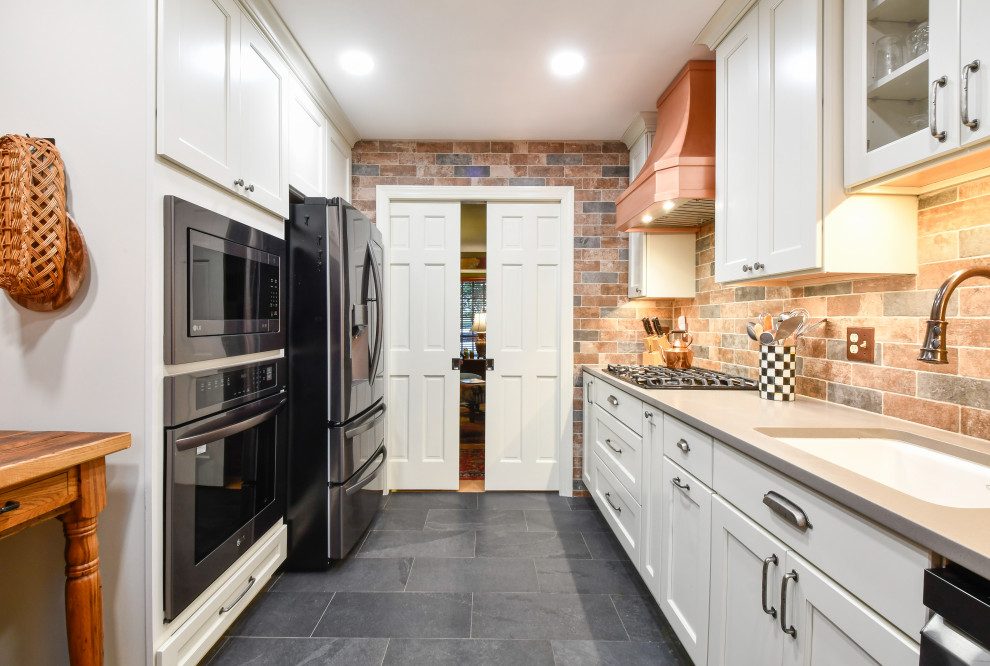 Inspiration for a mid-sized country u-shaped separate kitchen in DC Metro with a drop-in sink, recessed-panel cabinets, quartz benchtops, brick splashback, black appliances and no island.