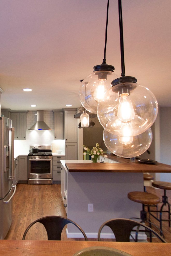 Mid-sized transitional l-shaped medium tone wood floor eat-in kitchen photo in Denver with a farmhouse sink, shaker cabinets, gray cabinets, quartz countertops, white backsplash, ceramic backsplash, stainless steel appliances and an island