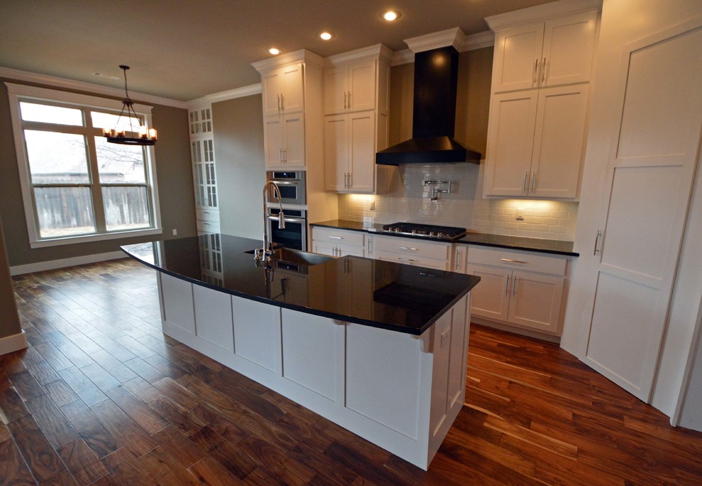 Mid-sized transitional l-shaped eat-in kitchen in Other with a farmhouse sink, shaker cabinets, granite benchtops, white splashback, subway tile splashback, stainless steel appliances, medium hardwood floors and with island.