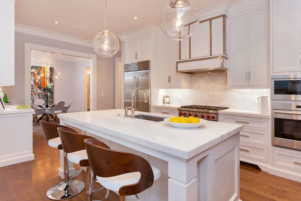 Transitional kitchen in New York with an undermount sink, recessed-panel cabinets, white cabinets, white splashback, stainless steel appliances, medium hardwood floors and with island.