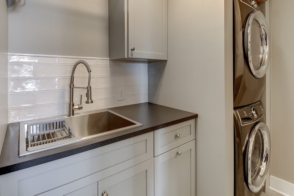 Small transitional single-wall dedicated laundry room in Dallas with a drop-in sink, shaker cabinets, grey cabinets, quartz benchtops, grey walls, a stacked washer and dryer, black benchtop, laminate floors and grey floor.