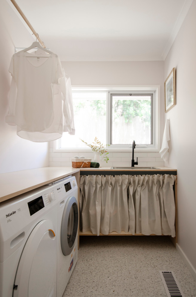 Photo of a small traditional l-shaped utility room in Melbourne with a drop-in sink, open cabinets, light wood cabinets, wood benchtops, white splashback, subway tile splashback, pink walls, a side-by-side washer and dryer, white floor and beige benchtop.