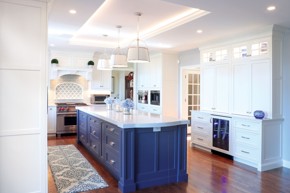 Modelo de cocina costera con armarios con paneles empotrados, puertas de armario azules, salpicadero azul, salpicadero de azulejos de cerámica, electrodomésticos con paneles y bandeja