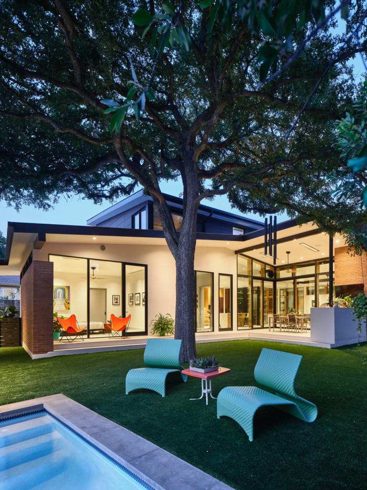 This is an example of a mid-sized midcentury two-storey brick white house exterior in Austin with a gable roof, a metal roof and a grey roof.