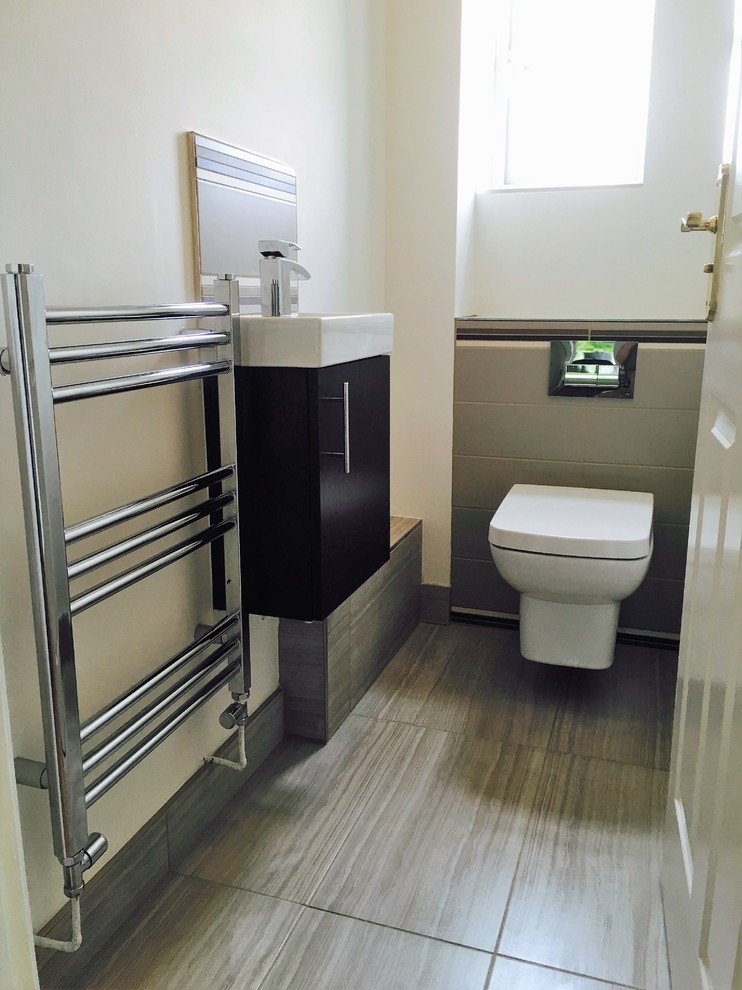 Photo of a small modern powder room in Other with flat-panel cabinets, dark wood cabinets, a wall-mount toilet, beige tile, ceramic tile, white walls, ceramic floors and a wall-mount sink.