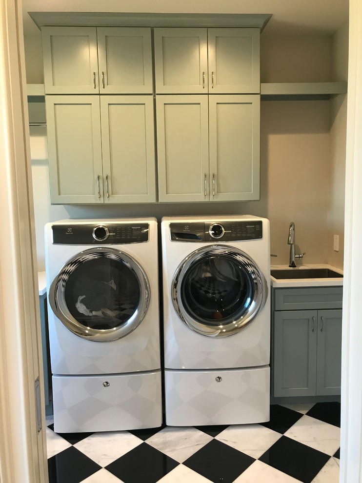 This is an example of a mid-sized modern galley dedicated laundry room in St Louis with an undermount sink, recessed-panel cabinets, green cabinets, solid surface benchtops, grey walls, marble floors, a side-by-side washer and dryer and black floor.