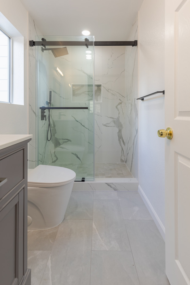 На фото: большая ванная комната в стиле модернизм с фасадами в стиле шейкер, серыми фасадами, душем в нише, унитазом-моноблоком, белой плиткой, белыми стенами, полом из керамической плитки, врезной раковиной, столешницей из искусственного кварца, серым полом, душем с раздвижными дверями, белой столешницей, тумбой под одну раковину, встроенной тумбой, мраморной плиткой, душевой кабиной и кирпичными стенами
