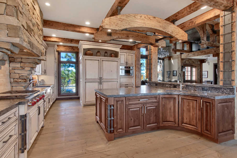 Design ideas for an expansive country l-shaped open plan kitchen in Denver with a farmhouse sink, raised-panel cabinets, white cabinets, granite benchtops, beige splashback, travertine splashback, panelled appliances, light hardwood floors, with island, beige floor and grey benchtop.