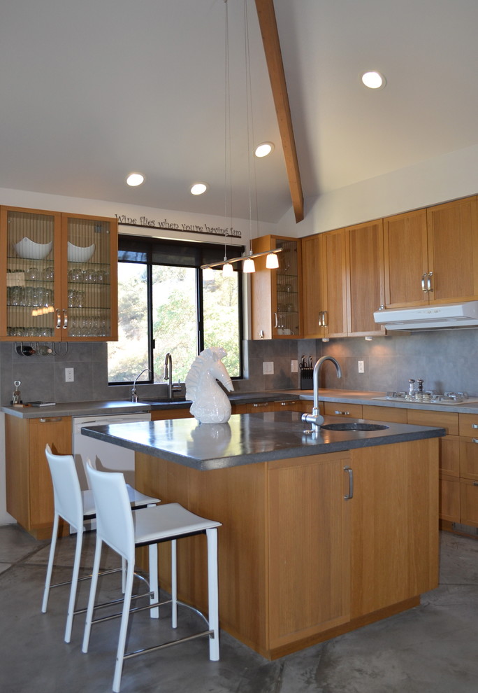 Small contemporary u-shaped open plan kitchen in San Luis Obispo with a single-bowl sink, glass-front cabinets, medium wood cabinets, concrete benchtops, grey splashback, ceramic splashback, white appliances, concrete floors and with island.
