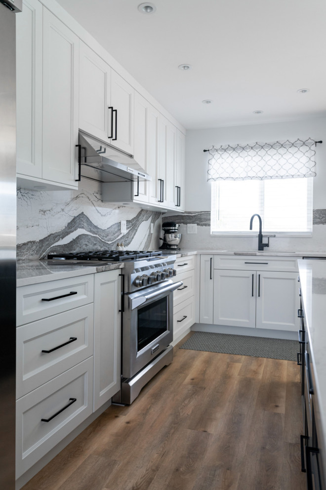 Example of a mid-sized transitional u-shaped medium tone wood floor and brown floor eat-in kitchen design with an undermount sink, recessed-panel cabinets, white cabinets, quartz countertops, white backsplash, stone slab backsplash, stainless steel appliances, an island and white countertops