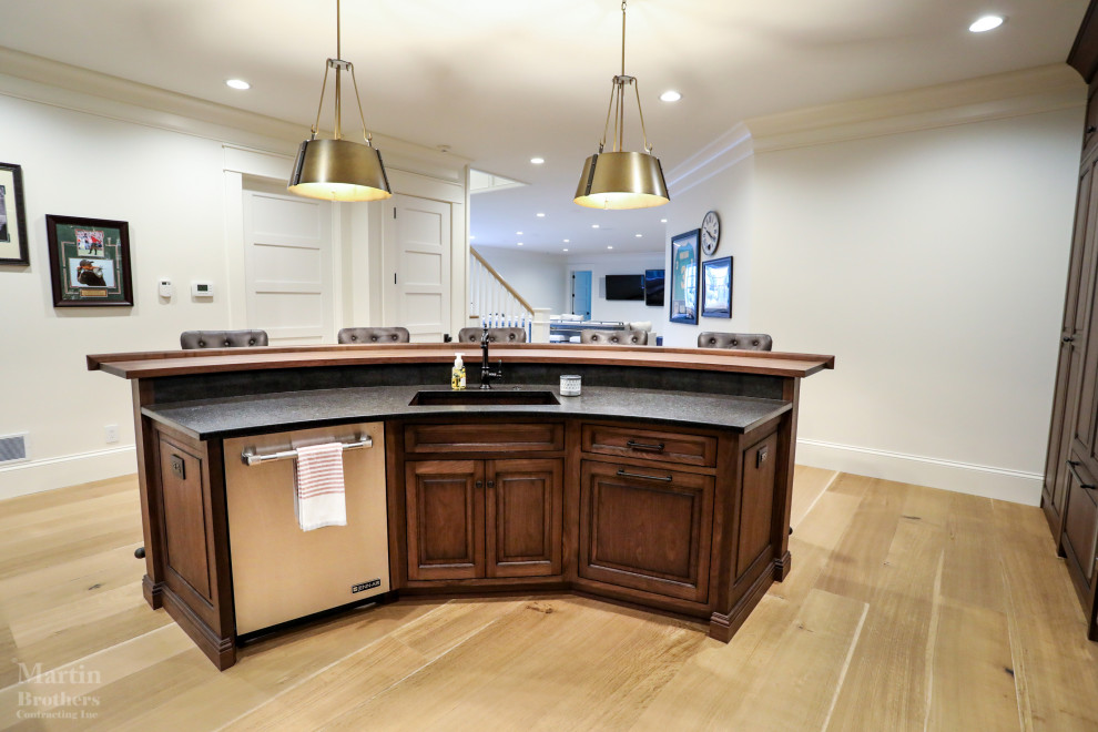Inspiration for a large traditional l-shaped wet bar in Other with an undermount sink, raised-panel cabinets, medium wood cabinets, brown splashback, granite splashback, light hardwood floors and black benchtop.
