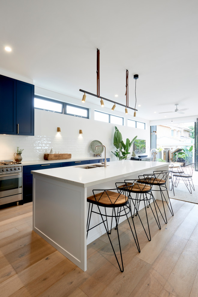 Photo of a contemporary galley eat-in kitchen in Sydney with an undermount sink, shaker cabinets, black cabinets, white splashback, stainless steel appliances, medium hardwood floors, with island, brown floor and white benchtop.