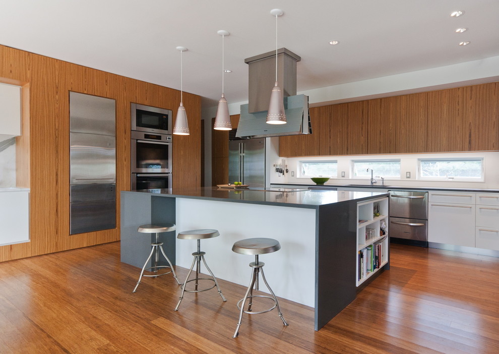 Inspiration for a contemporary u-shaped eat-in kitchen in New York with an undermount sink, flat-panel cabinets, medium wood cabinets, quartz benchtops, white splashback, stone slab splashback, stainless steel appliances, bamboo floors and with island.