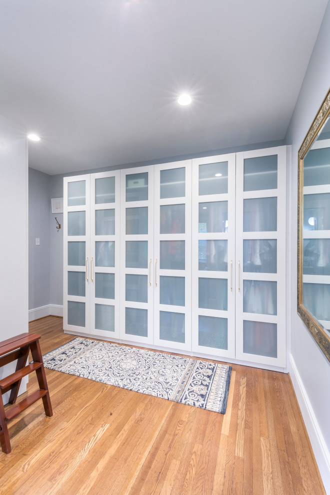 Inspiration for a large transitional gender-neutral dressing room in St Louis with glass-front cabinets, white cabinets, medium hardwood floors and brown floor.
