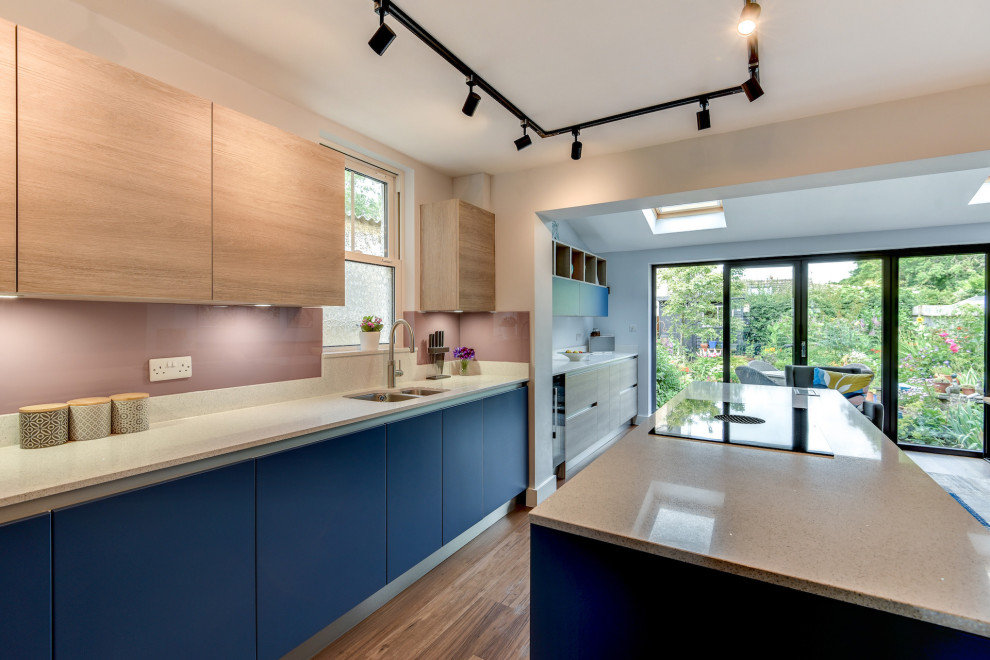 This is an example of a mid-sized beach style l-shaped eat-in kitchen in Sussex with a double-bowl sink, flat-panel cabinets, blue cabinets, quartzite benchtops, multi-coloured splashback, glass sheet splashback, black appliances, dark hardwood floors, with island, brown floor and white benchtop.