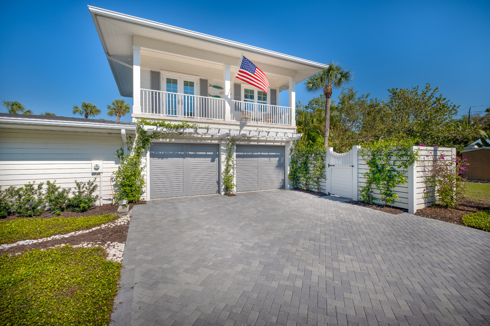 Design ideas for a mid-sized beach style two-storey white house exterior in Tampa with vinyl siding, a flat roof and a shingle roof.