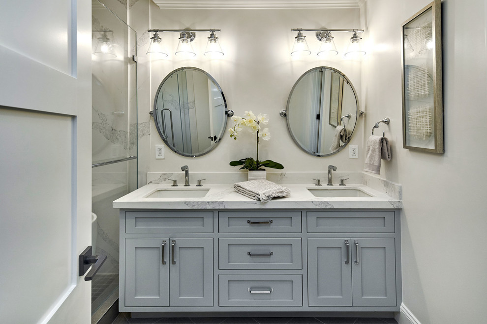 Design ideas for a mid-sized country master bathroom in San Francisco with shaker cabinets, grey cabinets, an alcove tub, a shower/bathtub combo, a one-piece toilet, white tile, stone slab, white walls, porcelain floors, an undermount sink, engineered quartz benchtops, grey floor, a hinged shower door and white benchtops.