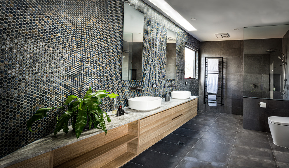 This is an example of a mid-sized modern master bathroom in Melbourne with glass-front cabinets, light wood cabinets, a corner shower, a one-piece toilet, gray tile, ceramic tile, grey walls, cement tiles, a console sink, wood benchtops, grey floor, an open shower and grey benchtops.