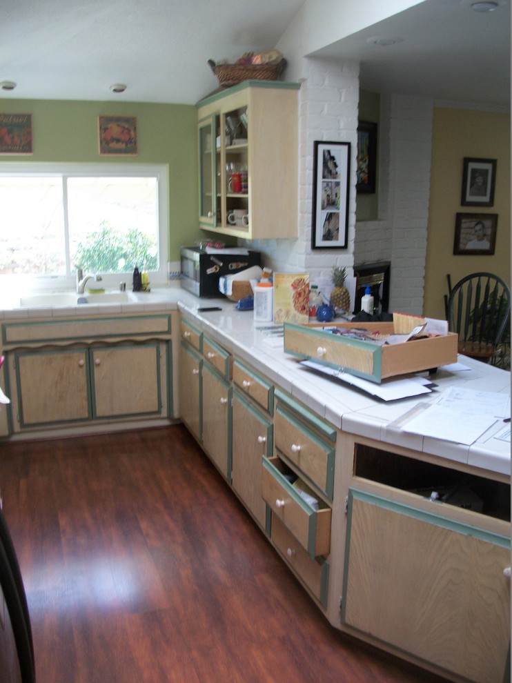 This is an example of a mid-sized transitional u-shaped eat-in kitchen in Sacramento with raised-panel cabinets, white cabinets, tile benchtops, white splashback, ceramic splashback, black appliances, a peninsula, a drop-in sink and dark hardwood floors.