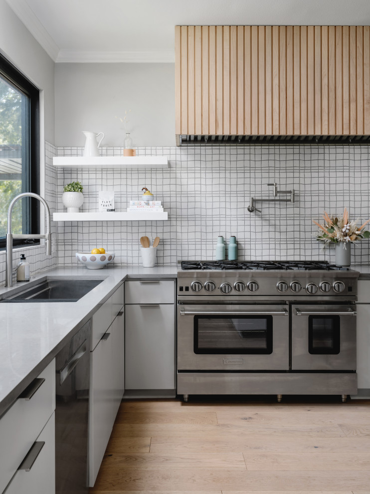 Inspiration for a mid-sized scandinavian galley eat-in kitchen in Austin with a drop-in sink, flat-panel cabinets, grey cabinets, quartz benchtops, white splashback, porcelain splashback, stainless steel appliances, medium hardwood floors, with island, brown floor and grey benchtop.