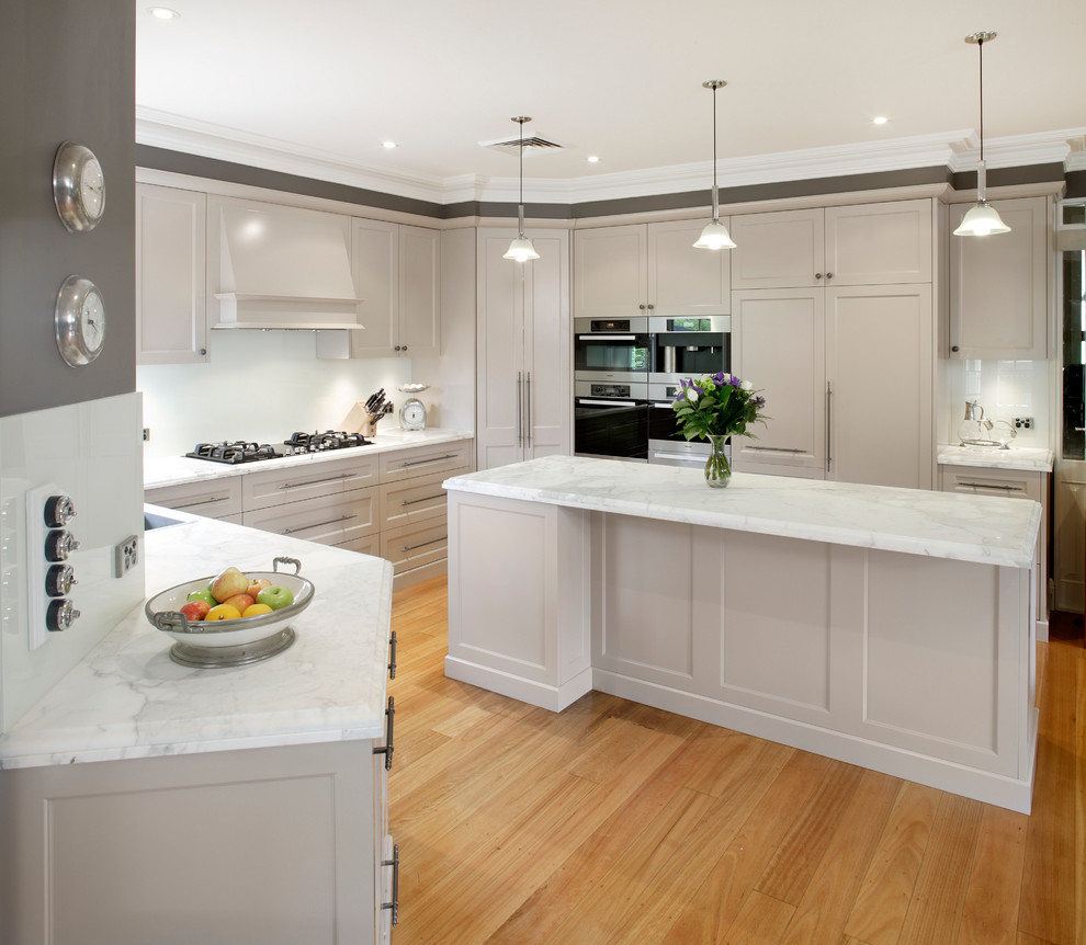 This is an example of a mid-sized transitional galley kitchen in Sydney with white cabinets, a double-bowl sink, shaker cabinets, marble benchtops, white splashback, glass sheet splashback, stainless steel appliances, medium hardwood floors and with island.