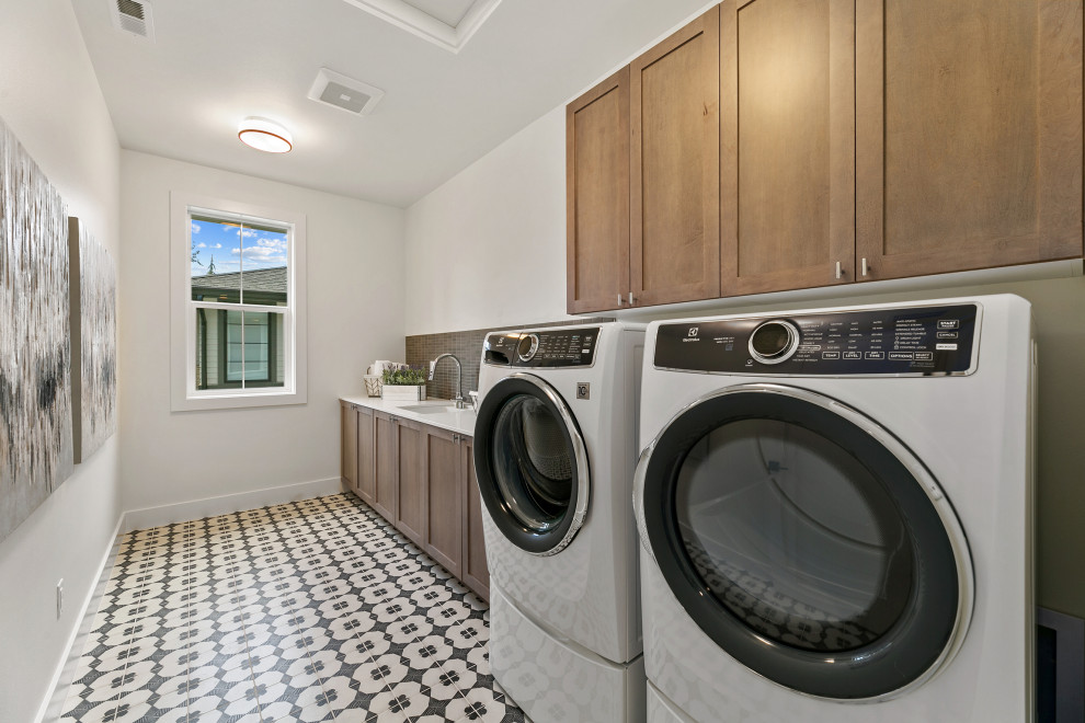 Photo of a large country galley dedicated laundry room in Seattle with an utility sink, recessed-panel cabinets, distressed cabinets, quartz benchtops, grey splashback, ceramic splashback, white walls, ceramic floors, a side-by-side washer and dryer, multi-coloured floor, white benchtop and vaulted.