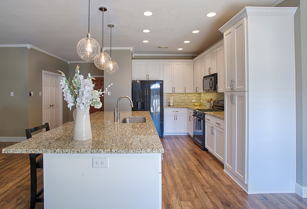 Photo of a mid-sized transitional l-shaped open plan kitchen in Austin with an undermount sink, shaker cabinets, white cabinets, granite benchtops, beige splashback, matchstick tile splashback, black appliances, medium hardwood floors and with island.