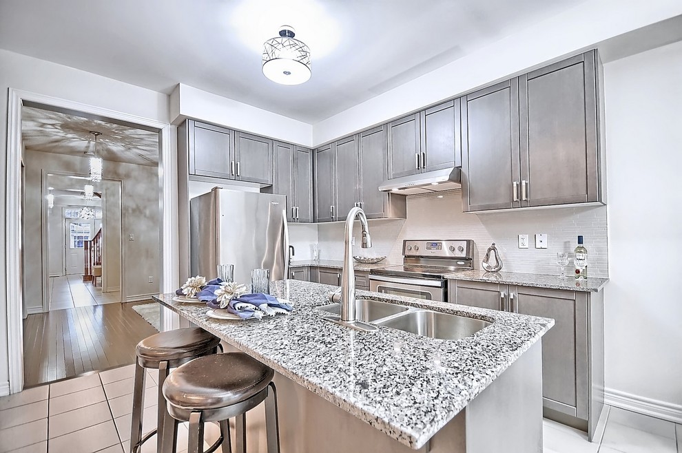 Open concept kitchen - mid-sized transitional l-shaped ceramic tile and beige floor open concept kitchen idea in Toronto with an undermount sink, shaker cabinets, gray cabinets, granite countertops, beige backsplash, mosaic tile backsplash, stainless steel appliances and an island