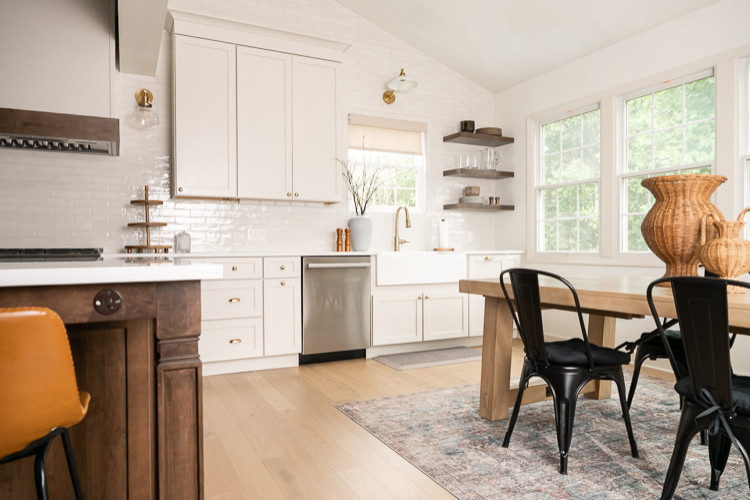 Example of a large transitional u-shaped light wood floor, brown floor and vaulted ceiling eat-in kitchen design with an undermount sink, shaker cabinets, white cabinets, quartz countertops, white backsplash, porcelain backsplash, stainless steel appliances, an island and white countertops