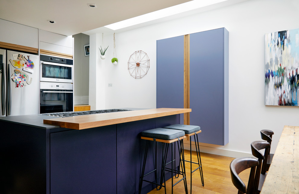 Photo of a large contemporary l-shaped eat-in kitchen in London with an integrated sink, flat-panel cabinets, purple cabinets, solid surface benchtops, white splashback, stone slab splashback, stainless steel appliances, medium hardwood floors, with island and brown floor.