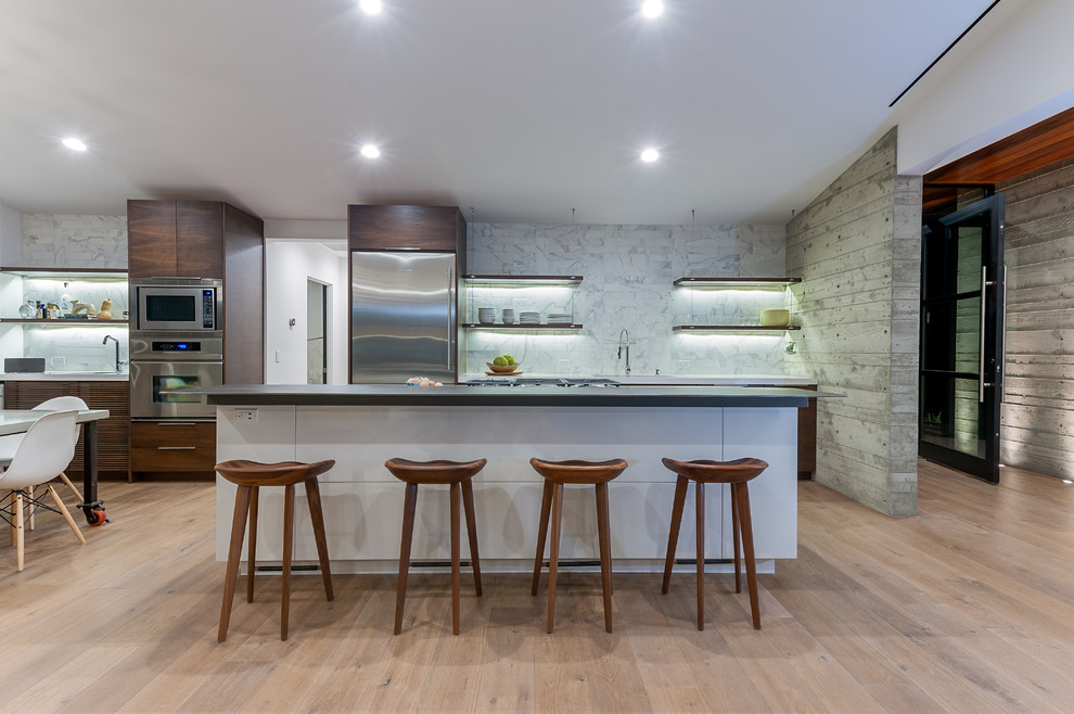 Photo of a large modern galley eat-in kitchen in San Diego with open cabinets, dark wood cabinets, white splashback, stainless steel appliances, light hardwood floors, with island, a drop-in sink, brown floor, solid surface benchtops and marble splashback.