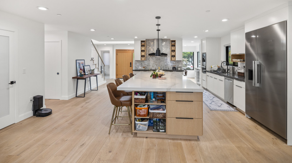Photo of a large modern eat-in kitchen in San Francisco with a drop-in sink, flat-panel cabinets, light wood cabinets, grey splashback, glass tile splashback, stainless steel appliances, light hardwood floors, with island, yellow floor and white benchtop.