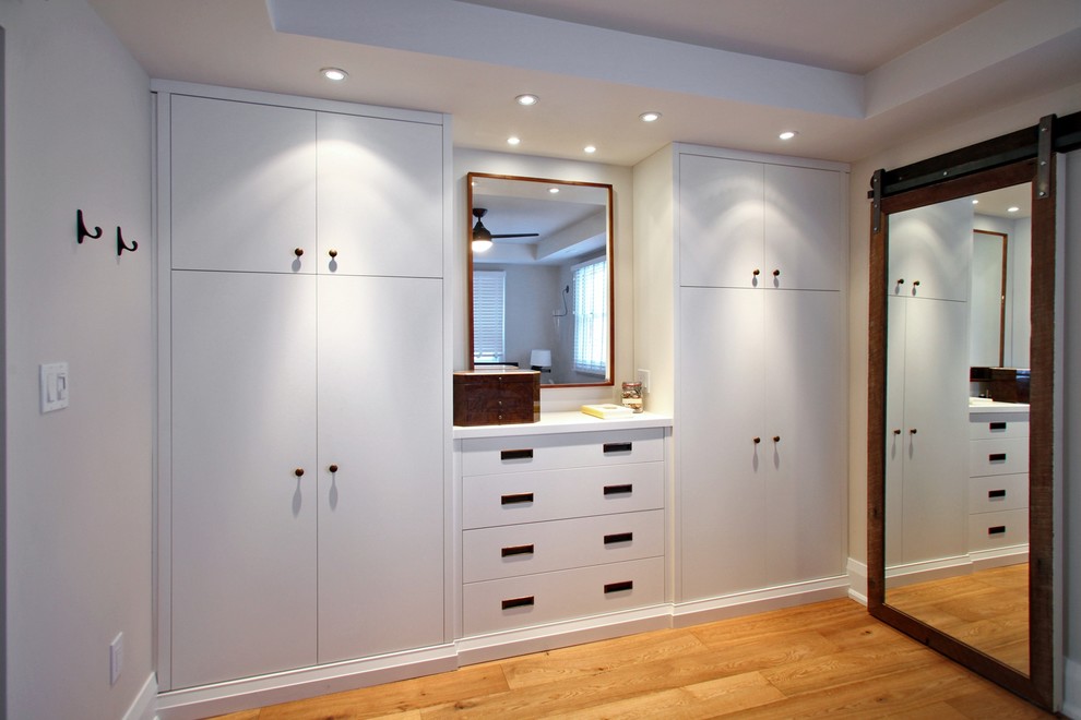 Design ideas for a large contemporary gender-neutral walk-in wardrobe in Toronto with flat-panel cabinets, white cabinets and light hardwood floors.